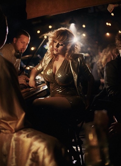 A woman in a glittering gold dress enjoying the atmosphere as musicians perform nearby, creating a glamorous vibe at revel supper club